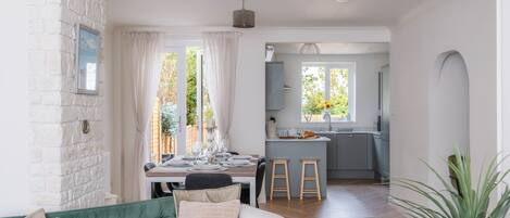 Un salon moderne avec un canapé vert, une table à manger dressée pour quatre personnes et une cuisine en arrière-plan.