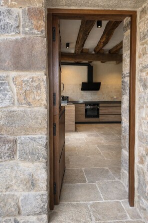 A stone-walled kitchen with a built-in oven and a wooden door leading to another room.