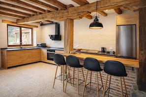 A modern kitchen with a wooden island, bar stools, a built-in oven, and a stainless steel refrigerator.
