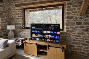 A television on a wooden stand in a stone-walled room with a window.