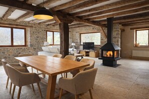 A rustic interior with a stone wall, wooden beams, a fireplace, a dining table, and comfortable seating. - Lores Peaks (Lores)