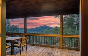 A wooden deck with a table and chairs, overlooking a forested landscape with a mountain in the distance. - Thoughtfully updated cabin with mountain views, screened decks, hot tub; sleeps 10 (Blue Ridge)