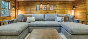 Ein modulares Sofa mit vielen Kissen, eine Holzwand mit gerahmten Motivationssprüchen und ein Fenster mit Blick auf Bäume.