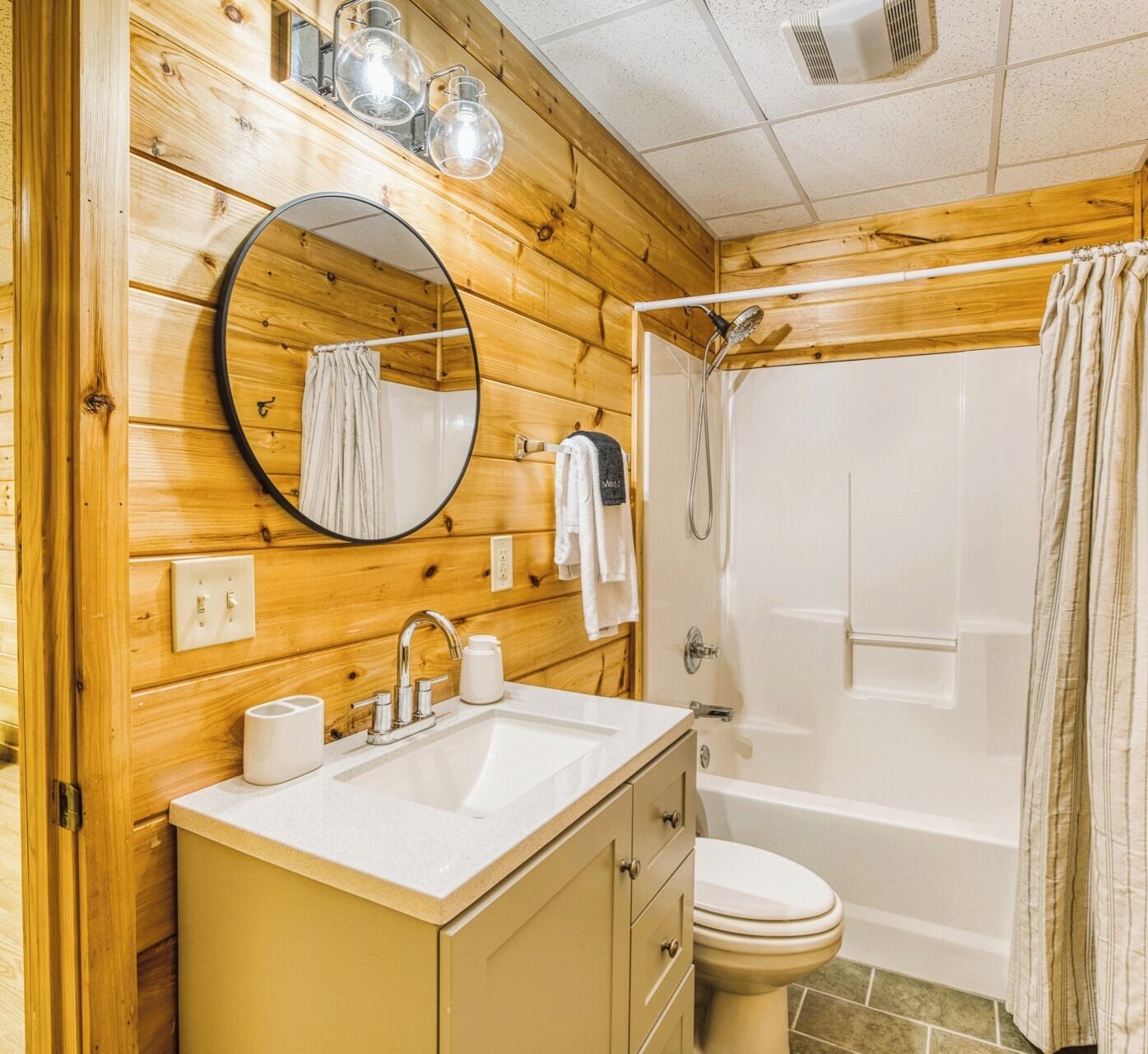 Une salle de bain aux murs lambrissés, équipée d’un lavabo, d’un miroir et de toilettes.
