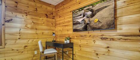 A room with wooden walls, a desk with a chair, a rug, and a framed picture of a rocky landscape.