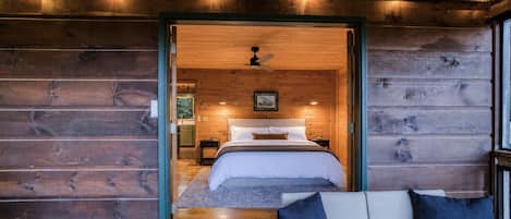 A wooden cabin interior with a bed, a small table, and a bench.