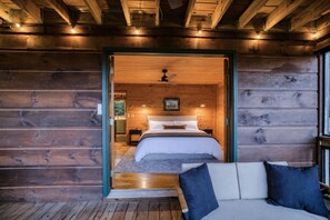 Ein Holzblockhaus-Innenraum mit einem Bett, einer Bank und Blick ins Freie.