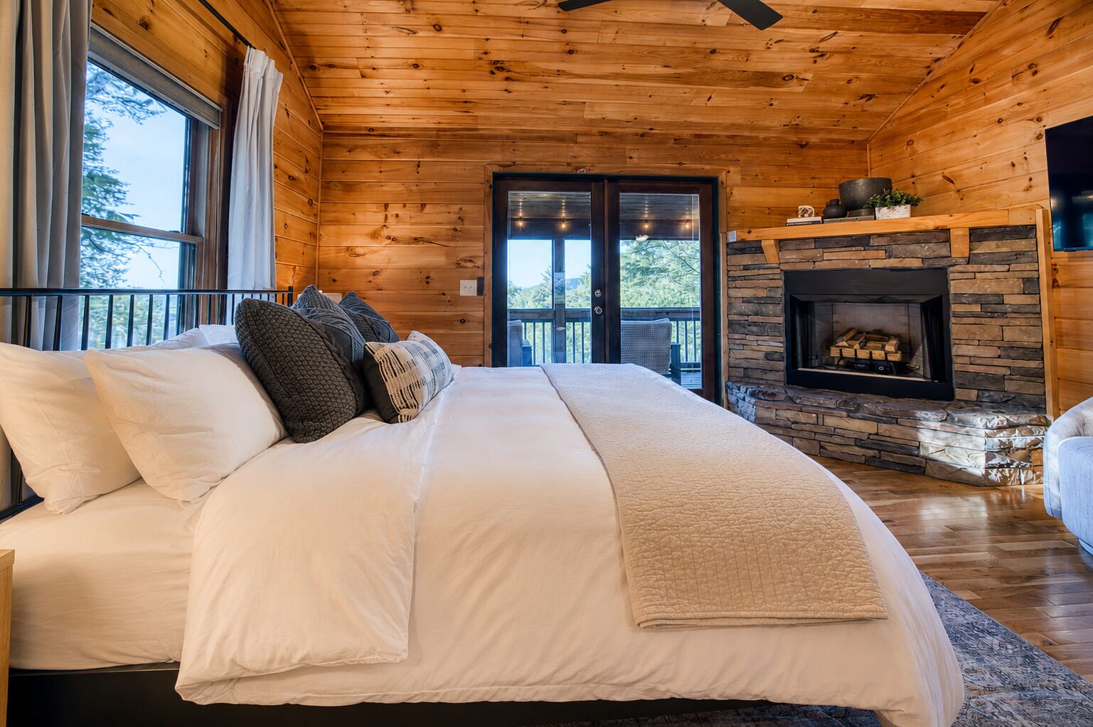 A wooden cabin bedroom with a large bed, a fireplace, and a balcony.