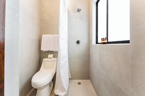 A bathroom with a toilet, a shower curtain, and a window with toiletries. - Suite with a Patio | Polanco | Relax (Ciudad de México)