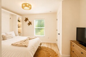 Une chambre à coucher comprenant un lit, un téléviseur, une fenêtre avec des stores, une étagère fixée au mur et un tapis tissé.