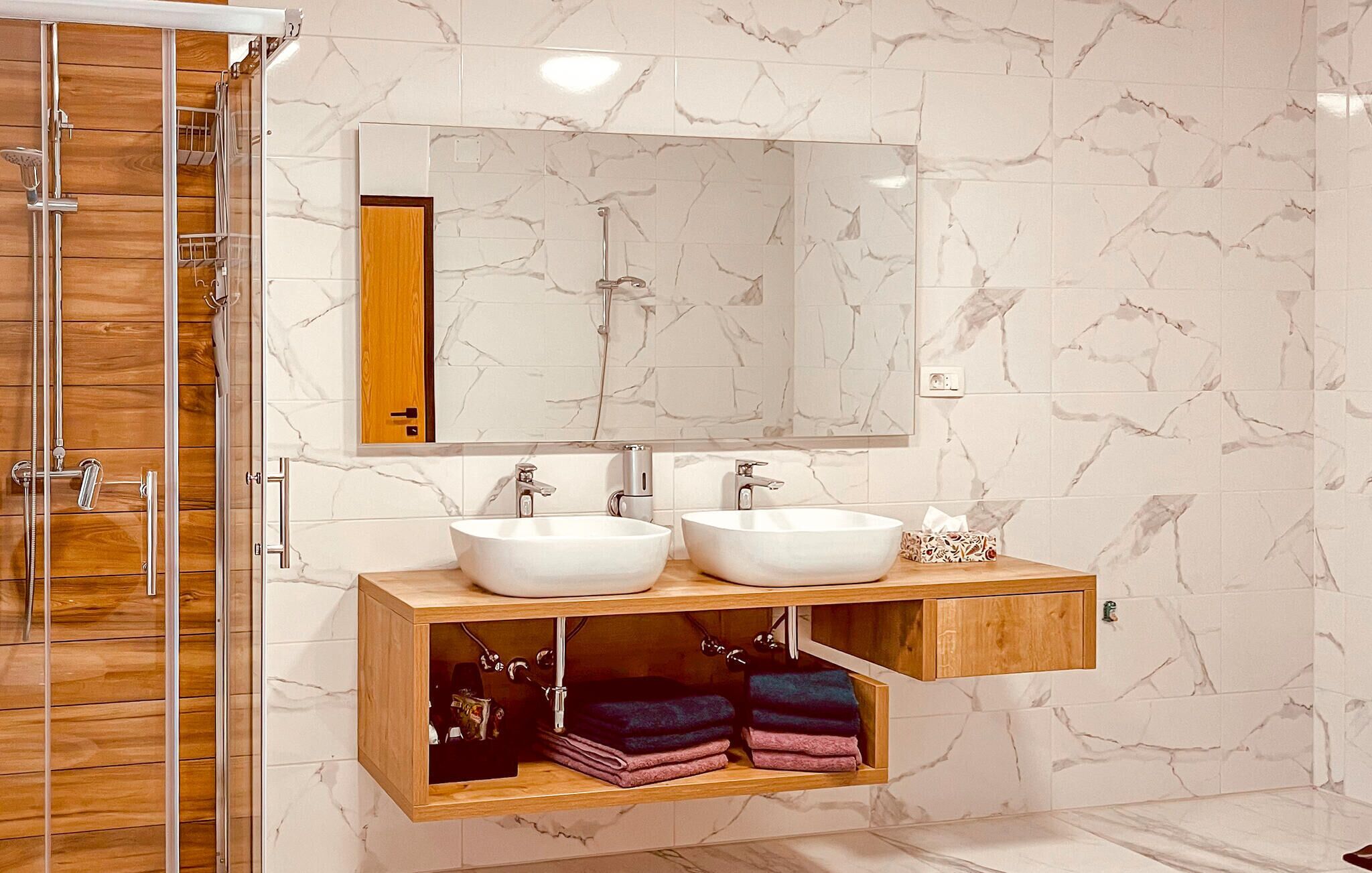Une salle de bain avec deux lavabos blancs, un meuble-lavabo en bois et un grand miroir au-dessus des lavabos.