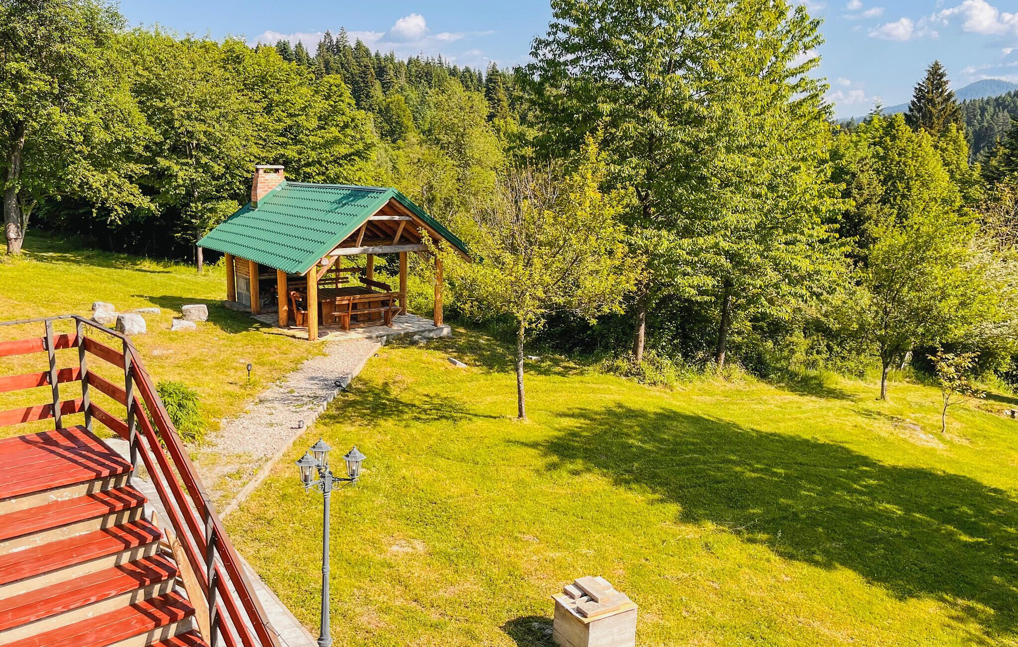 A wooden cabin with a green roof, surrounded by lush greenery and a stone pathway leading to it.