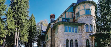A historic stone building with a turret, surrounded by tall trees.