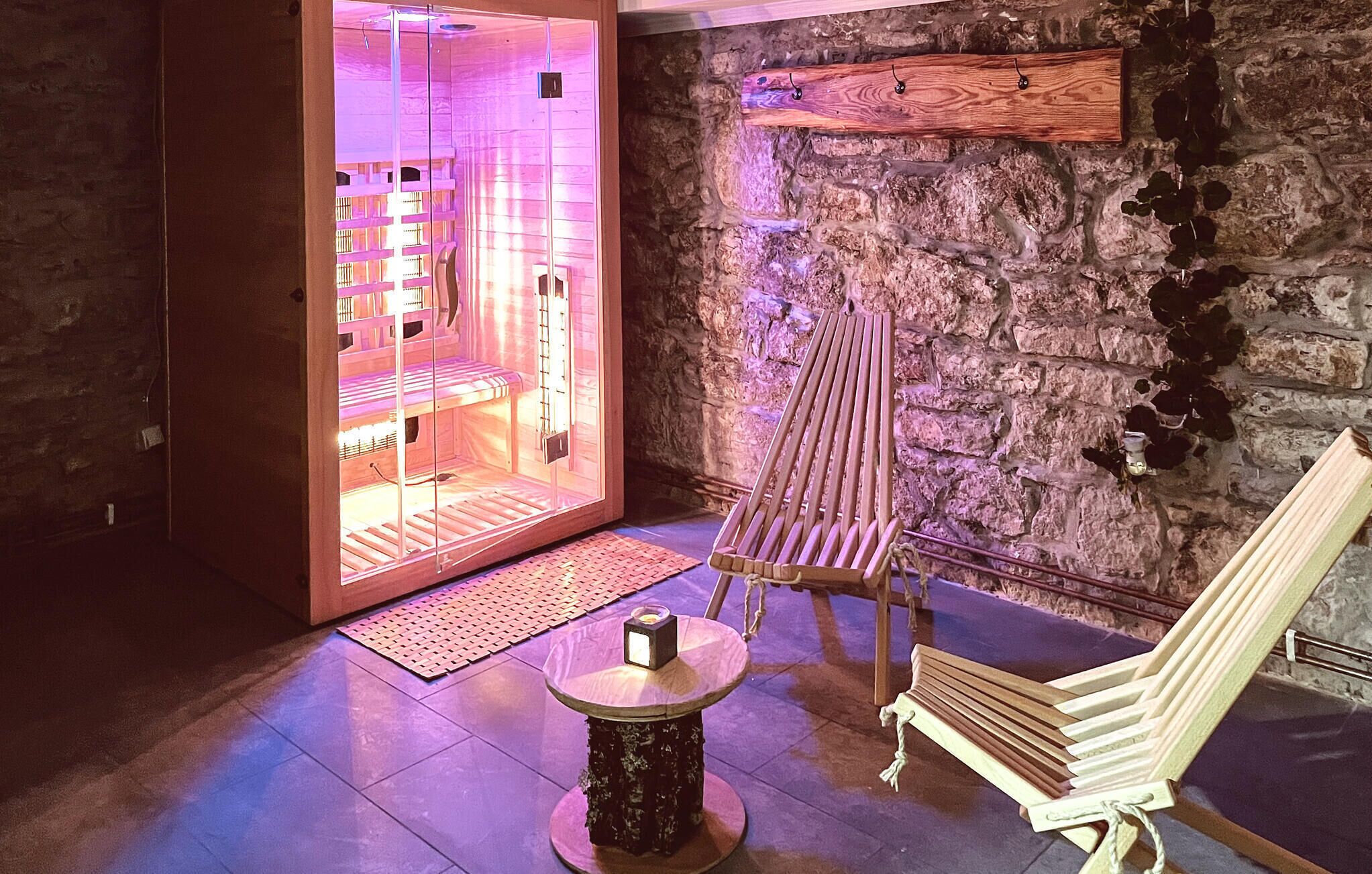 A spa room with a stone wall, a wooden bench, a massage table, and a small table with a candle.