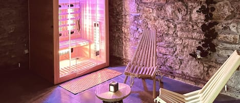 Ein Wellnessraum mit Steinwand, einer Holzbank, einem Massagetisch und einem kleinen Tisch mit einer Kerze.