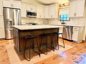 A modern kitchen with stainless steel appliances, a marble countertop, and wooden stools.