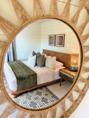 A bedroom with a bed, pillows, a bedside table with a lamp, and a mirror on the wall.