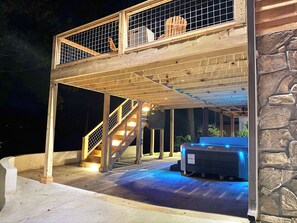 A two-story wooden structure with a stone wall, a hot tub, and a staircase.