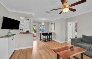 A modern living room with a flat-screen TV, a wooden coffee table, and a ceiling fan. - 3 min walk to the best sunsets on the beach! (St. Pete Beach)
