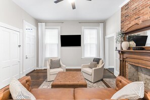 Ein Wohnzimmer mit zwei Sesseln, einer Couch, einem Kamin und einem an der Wand befestigten Flachbildfernseher.