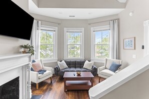 Ein Wohnzimmer mit Kamin, einer Sofagarnitur, einem Couchtisch und großen Fenstern.