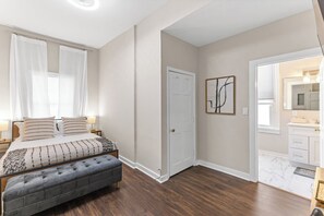 A bedroom with a bed, bedside tables, a bench, a door, and a bathroom with a vanity and mirror. - 6br, 4ba, sleeps 16 - DT Wilm, Walk to everything! (Wilmington)