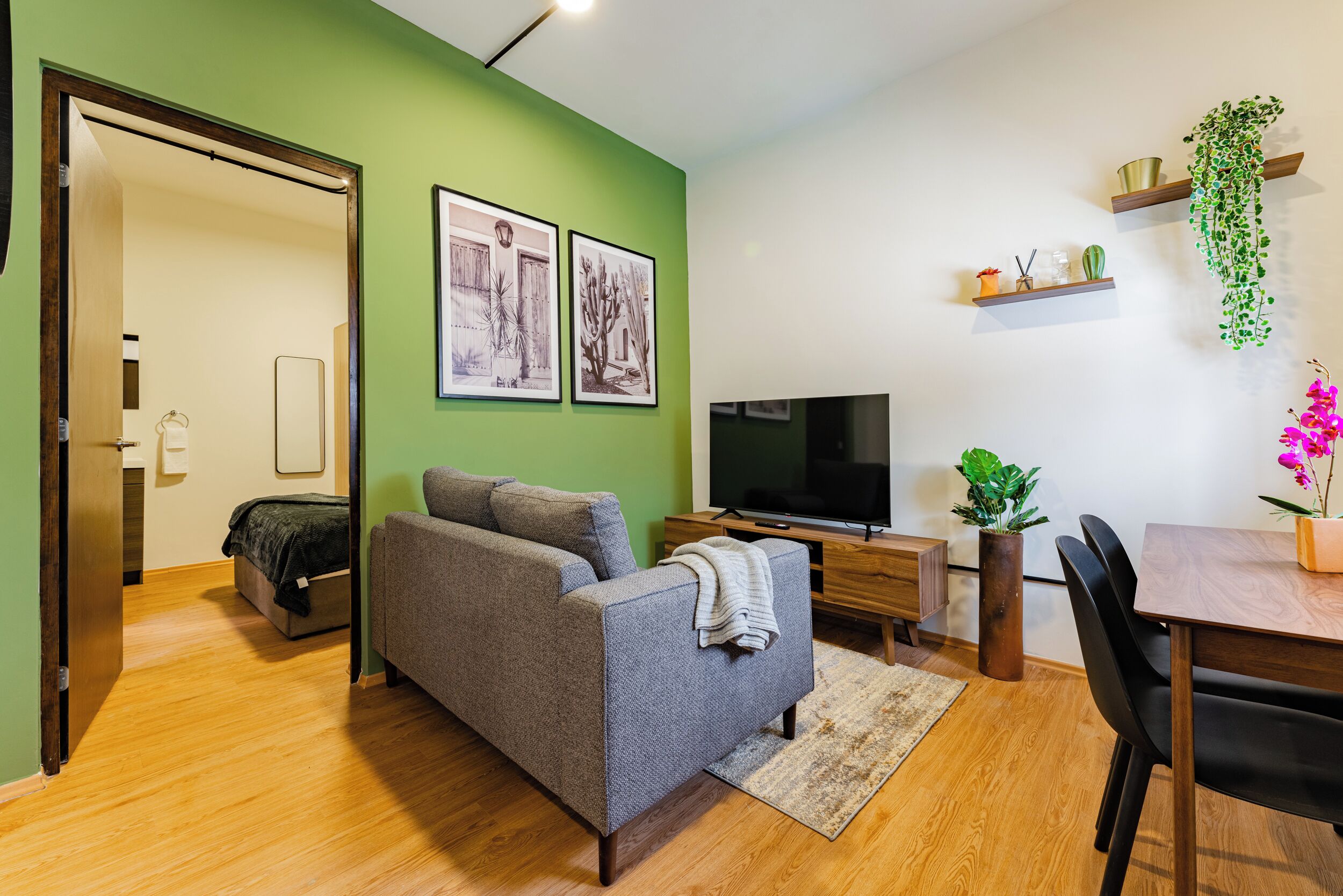 A modern living room with a grey sofa, a flat-screen TV, and a dining area with a wooden table and chairs.