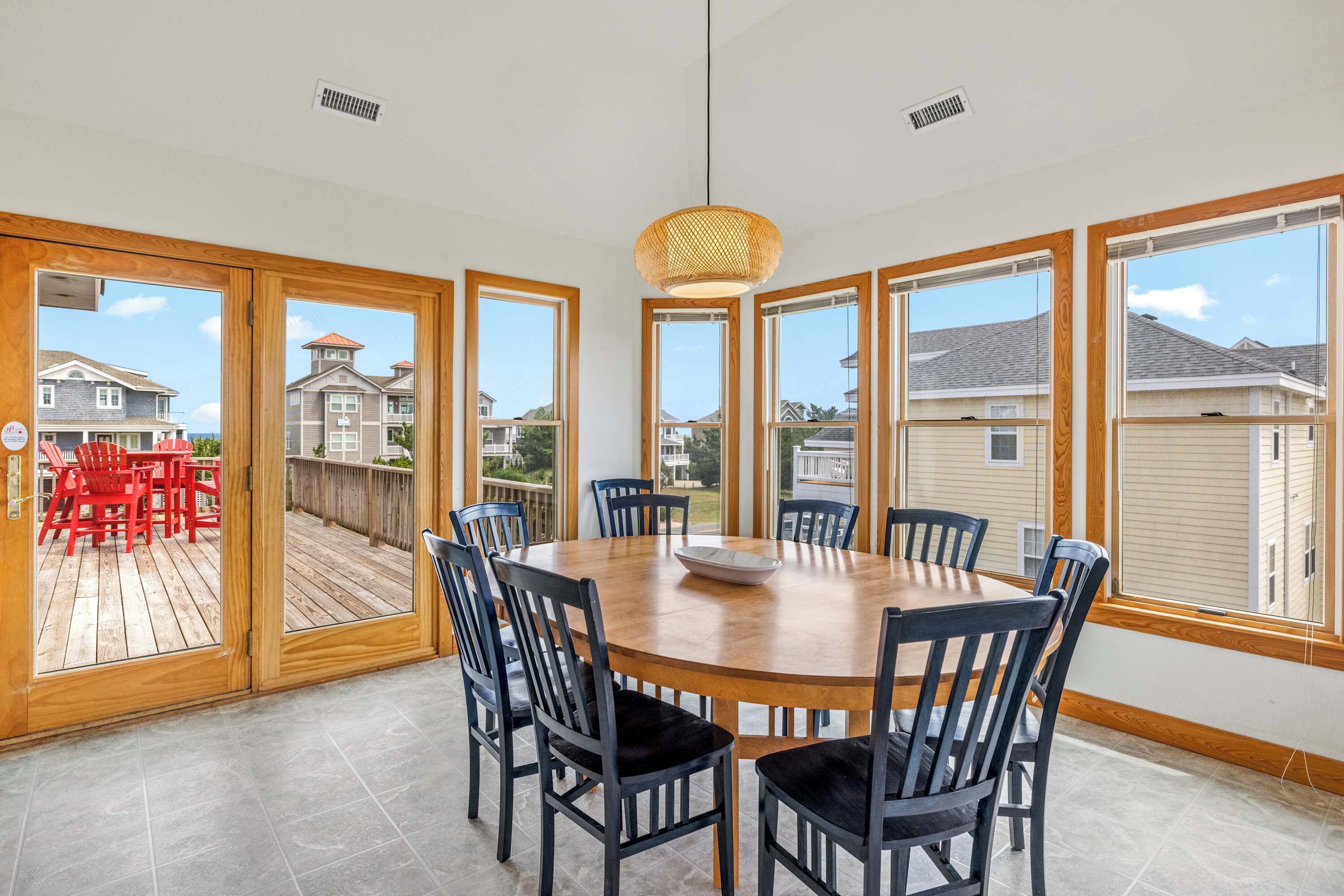 A dining area with a round table and chairs, large windows, and a view of the neighborhood.