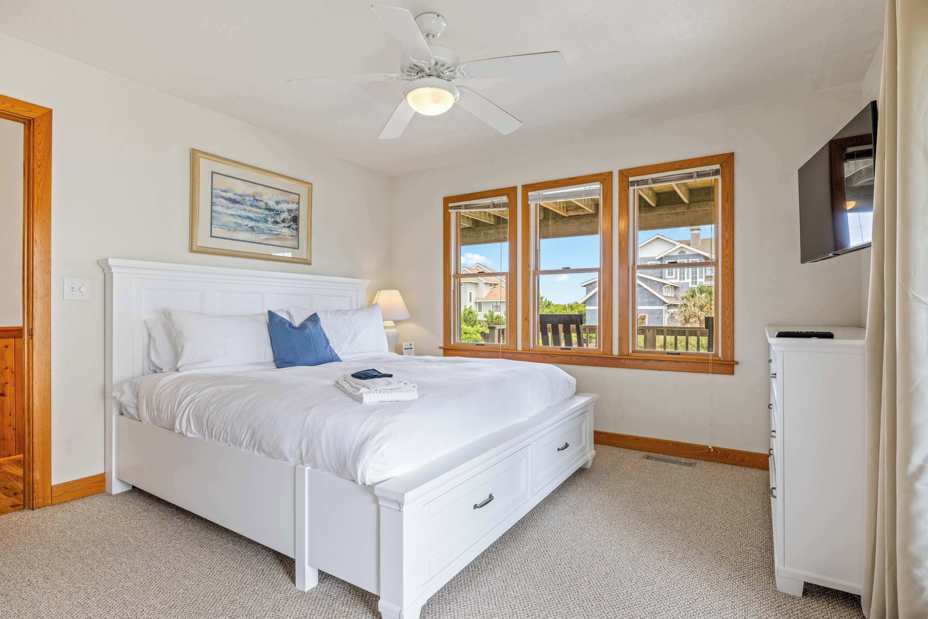 A bedroom with a bed, a ceiling fan, a window with a view, and a TV mounted on the wall.