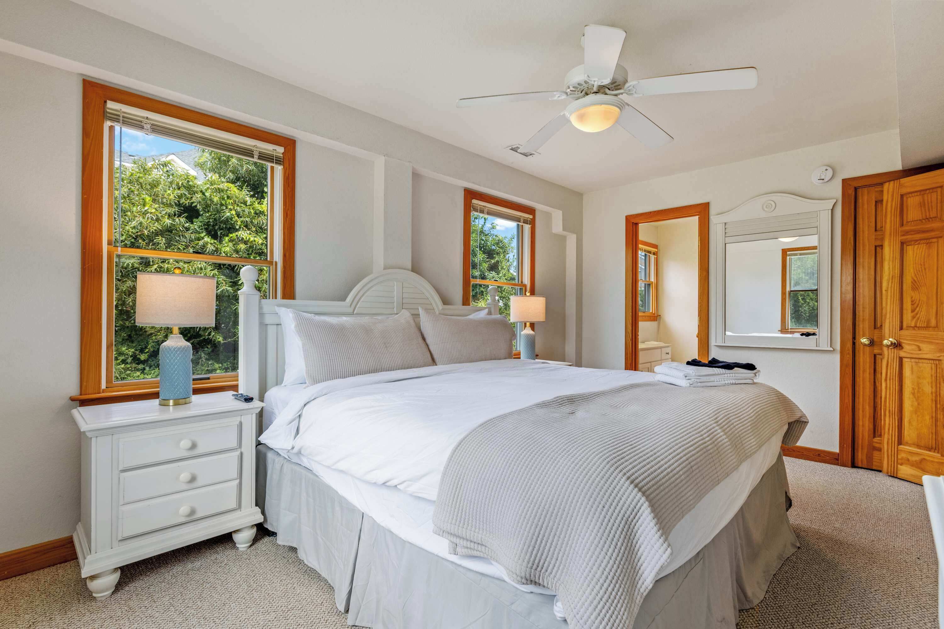 A bedroom with a bed, nightstands, a ceiling fan, and large windows.