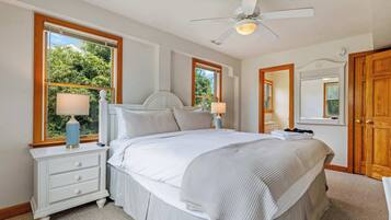 A bedroom with a bed, nightstands, a ceiling fan, and large windows.