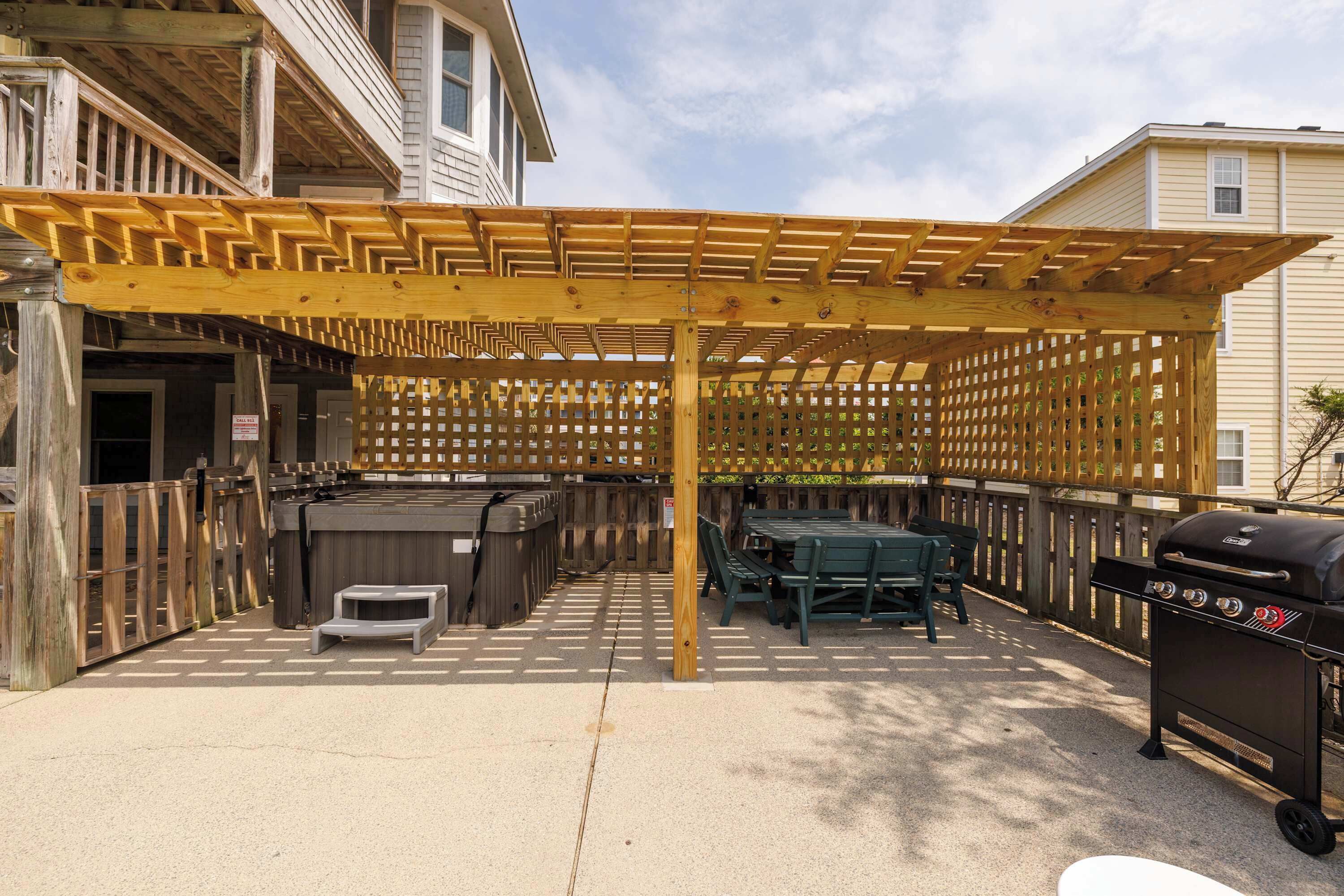 Ein Außenbereich mit einer Holzpergola, einem Whirlpool, einem Grill und einem Tisch mit Stühlen.