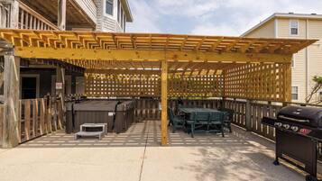 Ein Außenbereich mit einer Holzpergola, einem Whirlpool, einem Grill und einem Tisch mit Stühlen.