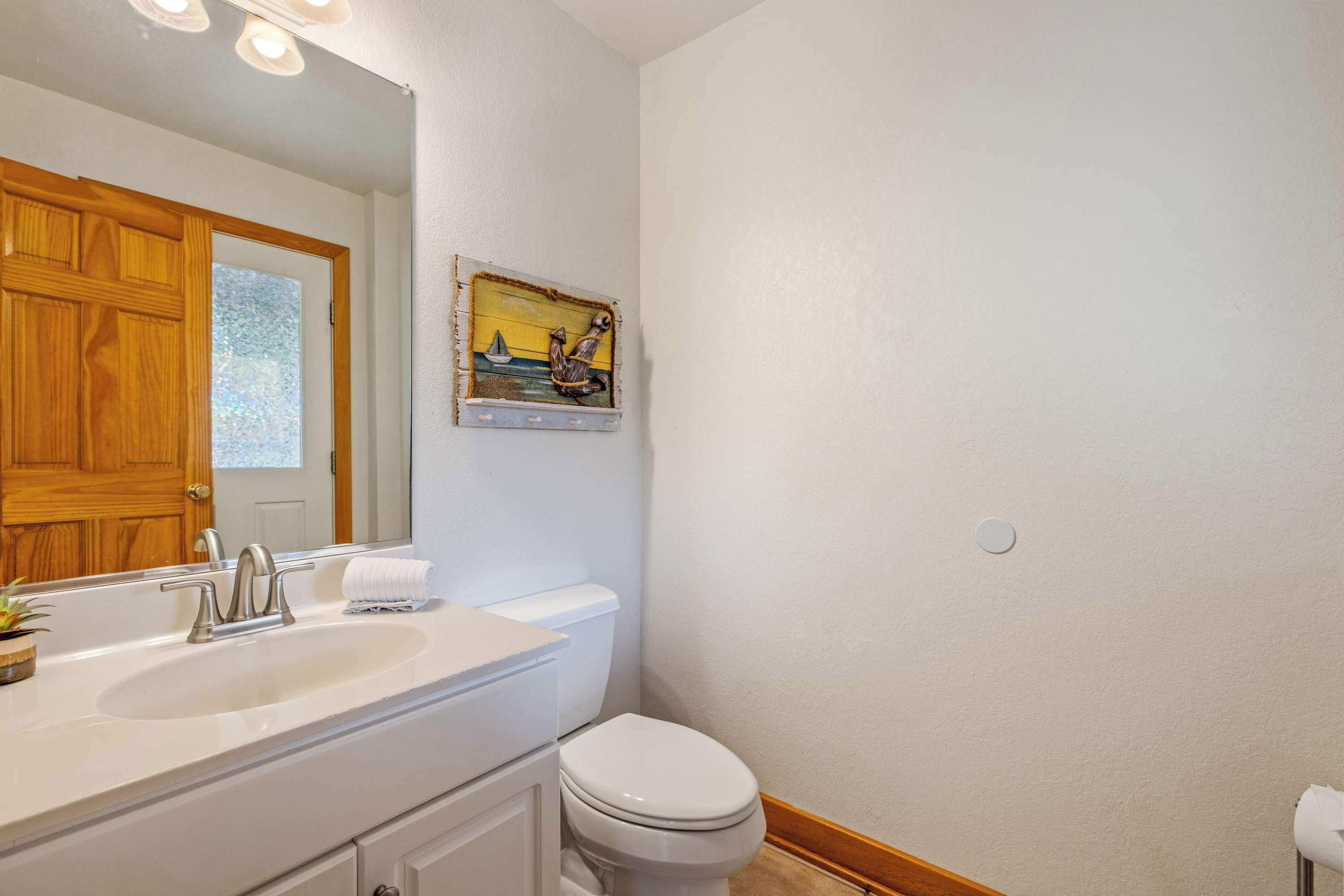 Une salle de bain avec une porte en bois, un lavabo blanc doté d’un robinet moderne, des toilettes et un tableau représentant un voilier, accroché au mur.