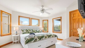 Una camera da letto con un letto, una scrivania, una sedia, un ventilatore a soffitto e finestre con stipiti in legno.