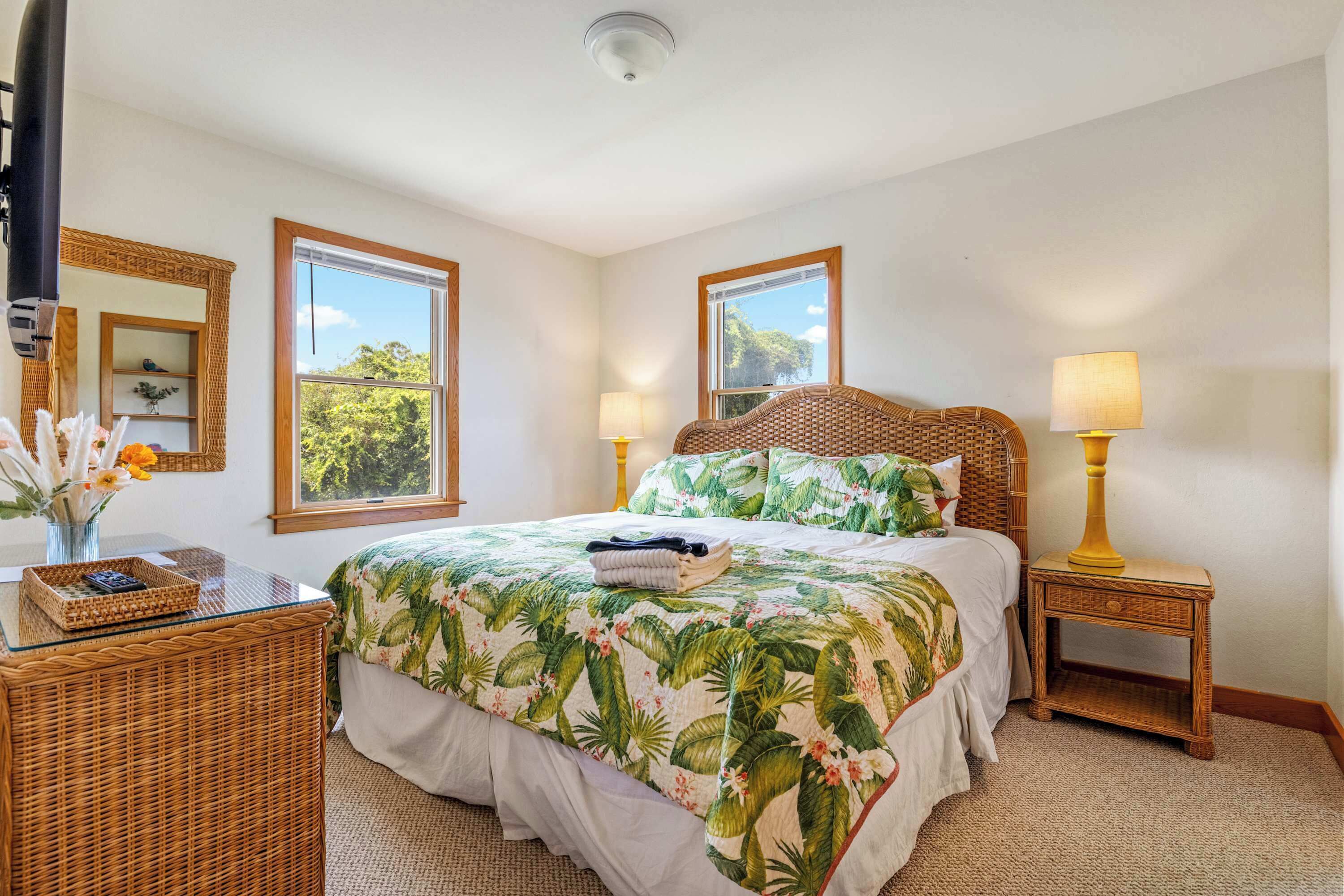 A bedroom with a bed, two bedside tables, a mirror, and a window with a view of trees.