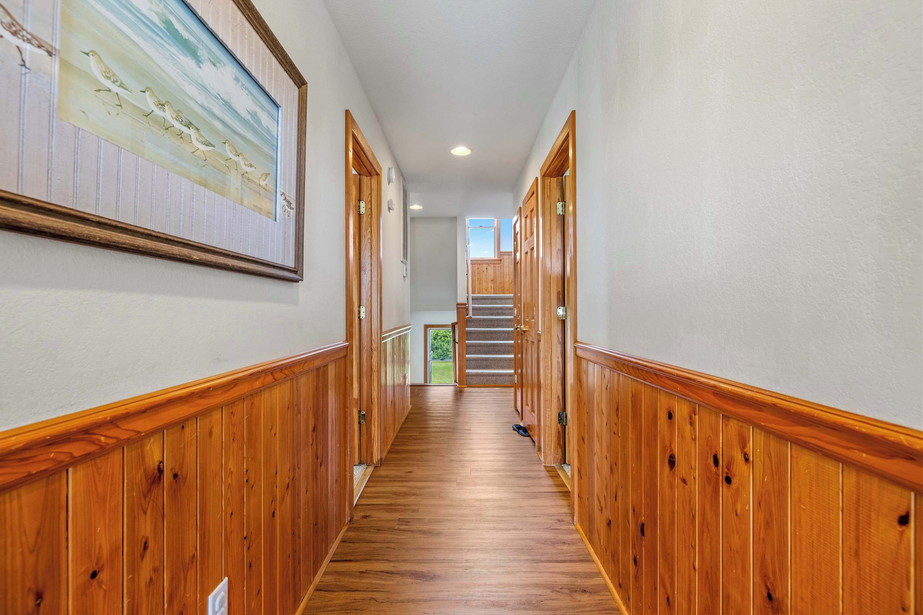 A wooden-paneled hallway with a framed painting on the wall, leading to a staircase.