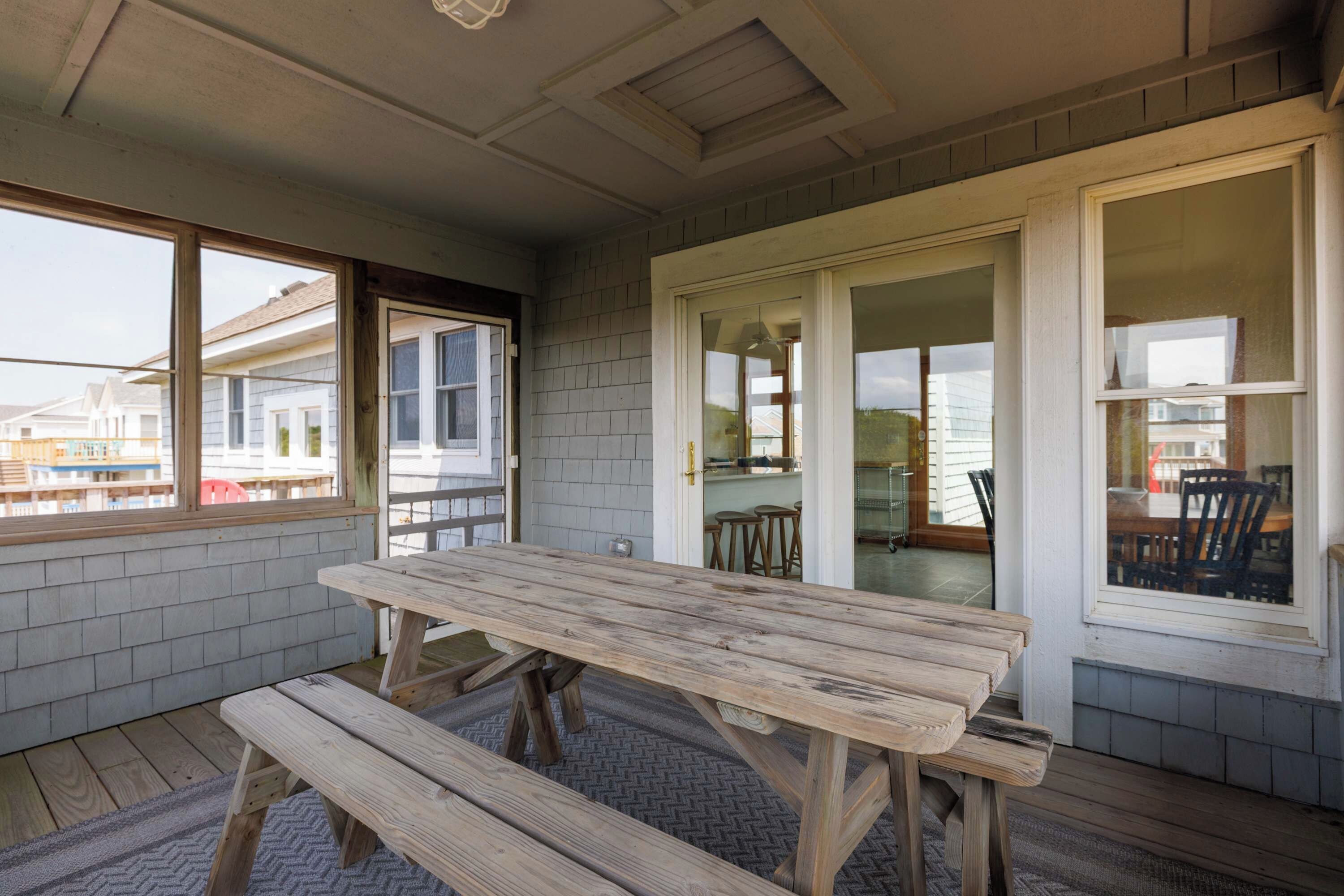 An outdoor patio with a wooden table and benches, a sliding glass door leading to a kitchen area, and a view of neighboring houses.