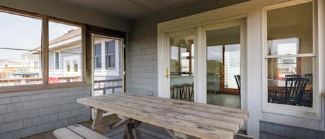 An outdoor patio with a wooden table and benches, a sliding glass door leading to a kitchen area, and a view of neighboring houses.
