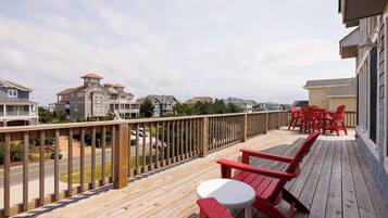 A wooden deck with red chairs and a white table, overlooking a residential area with houses and a road.