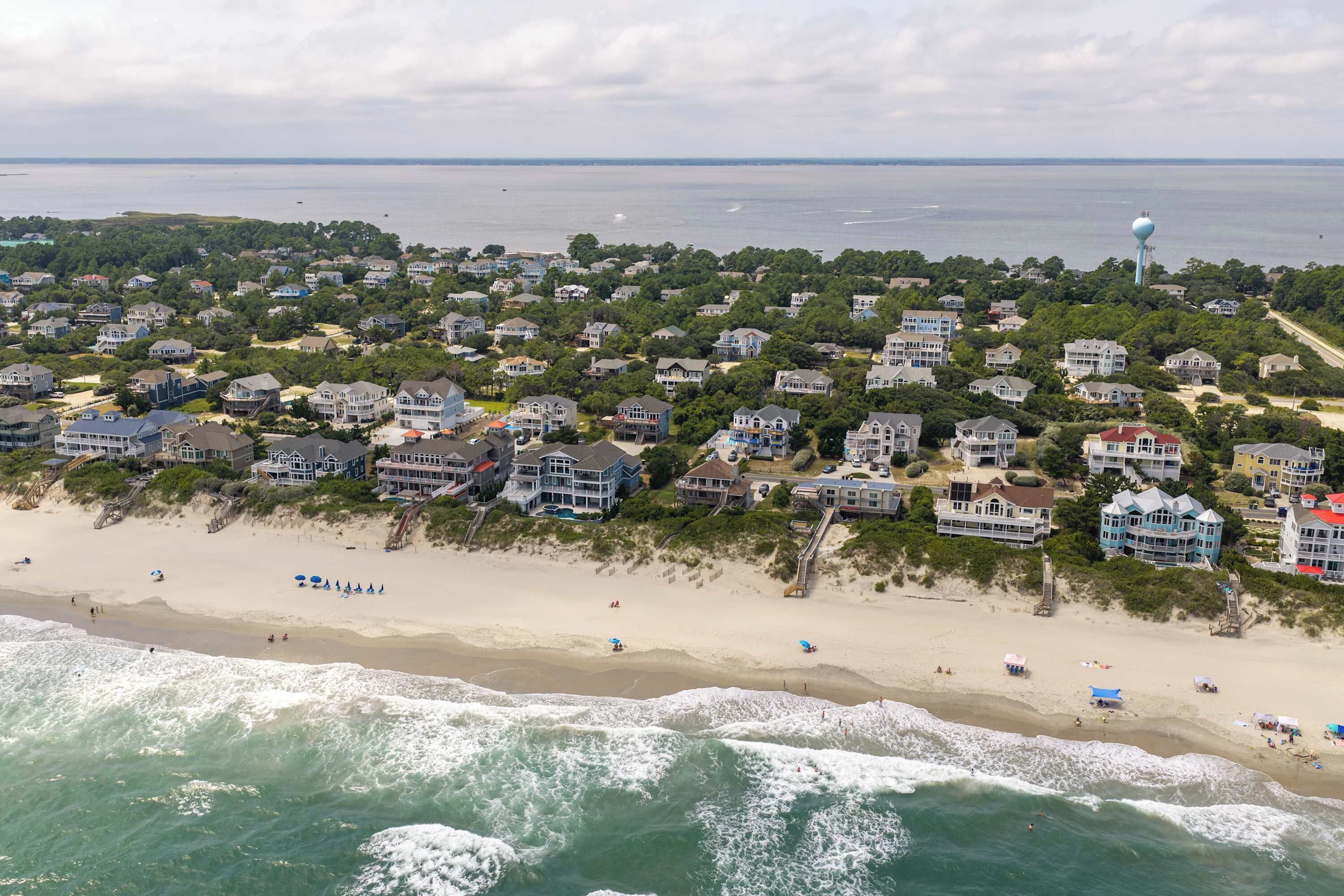 Una zona residenziale sul litorale con case affacciate sulla spiaggia, una spiaggia sabbiosa e onde oceaniche.