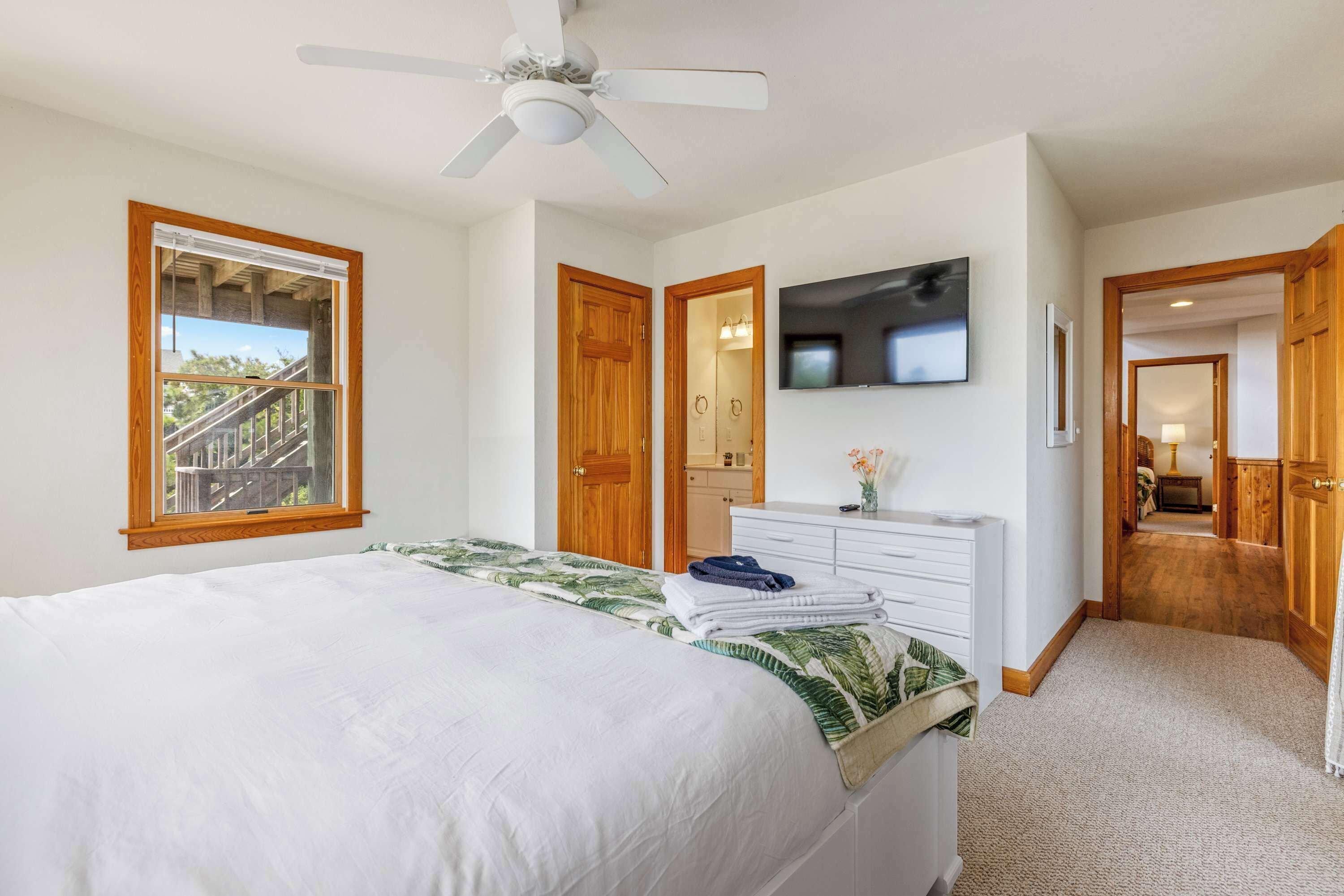 Une chambre à coucher avec un lit, un ventilateur de plafond, une télévision et une vue sur un balcon.