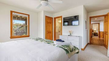 Un dormitorio con cama, ventilador de techo, televisor y vista a un balcón.