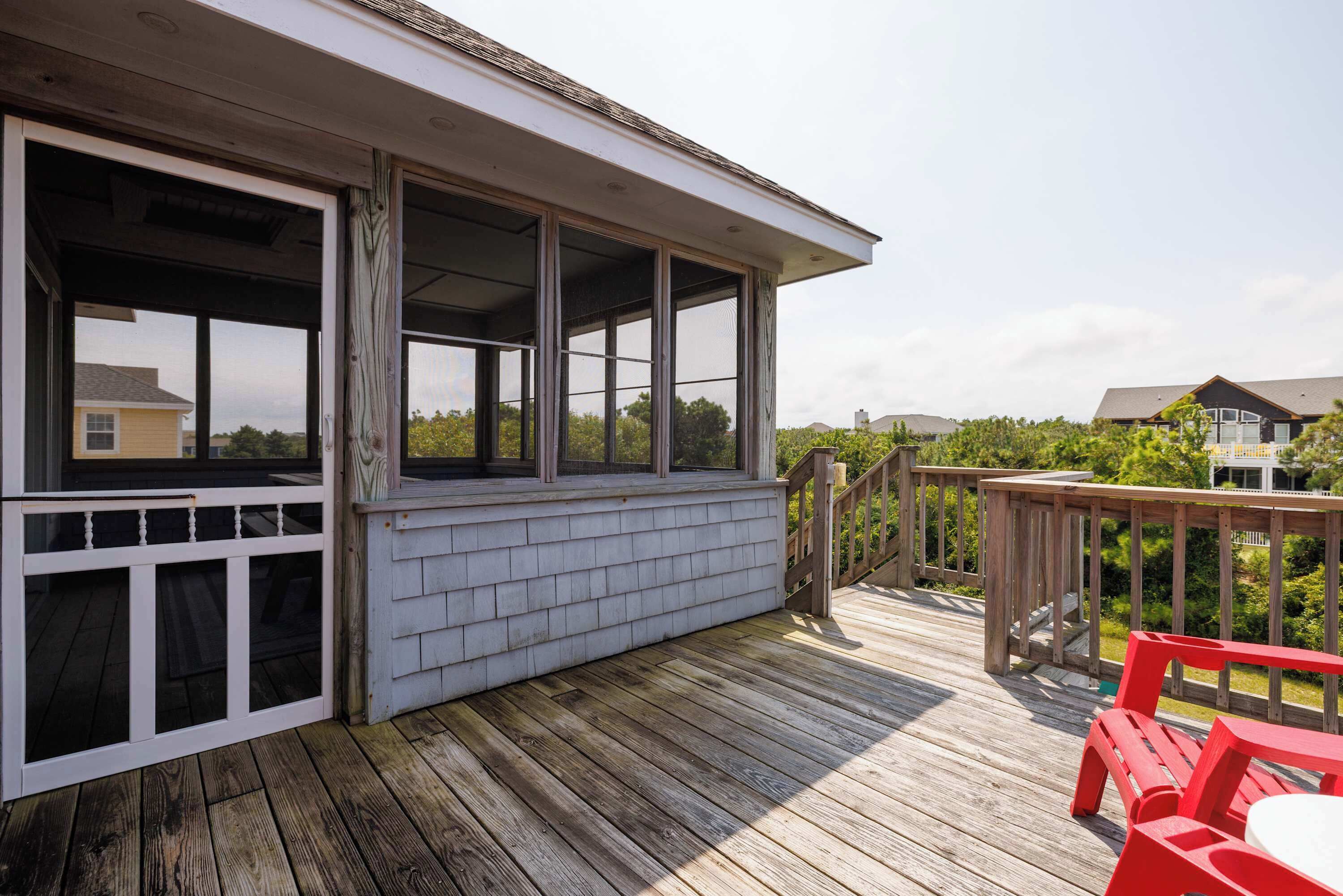 A wooden deck with a covered area, a railing, and a view of the surrounding neighborhood.