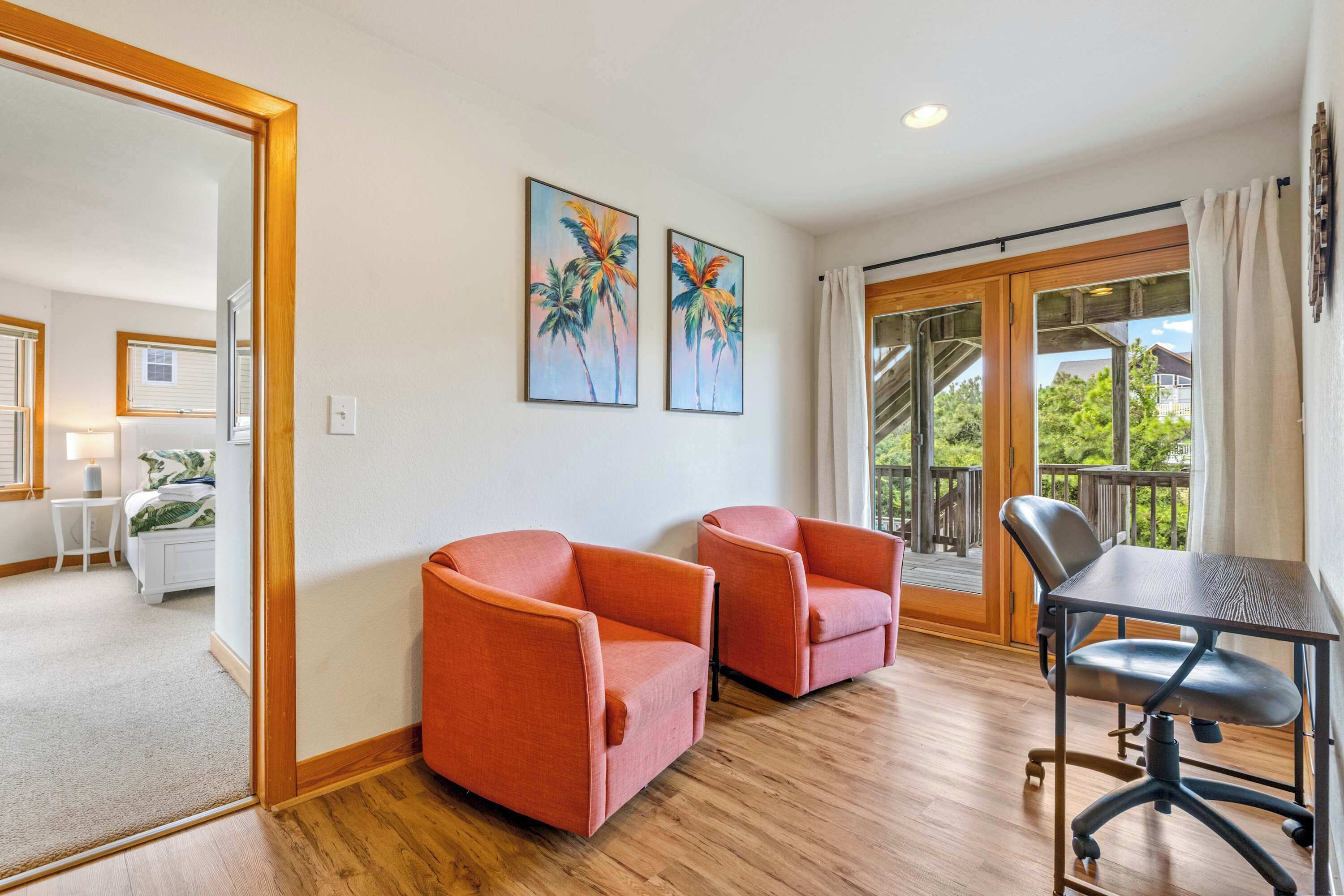 A room with two orange chairs, a table, and a view of a balcony with a wooden deck.