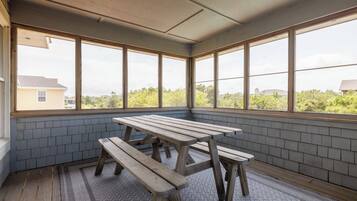 A sunroom with a wooden table and benches, large windows, and a view of greenery and buildings.