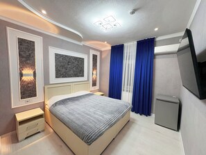 A modern bedroom with a bed, bedside tables, a TV, and a small cabinet. - Guest-House Grand (Tashkent)