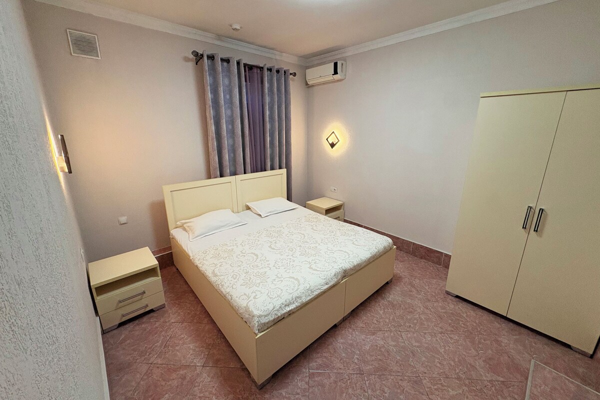 Una camera da letto con un letto, comodini, un armadio, una finestra con tende e un condizionatore d'aria a parete.