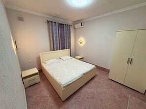 Una camera da letto con un letto, comodini, un armadio, una finestra con tende e un condizionatore d'aria a parete.