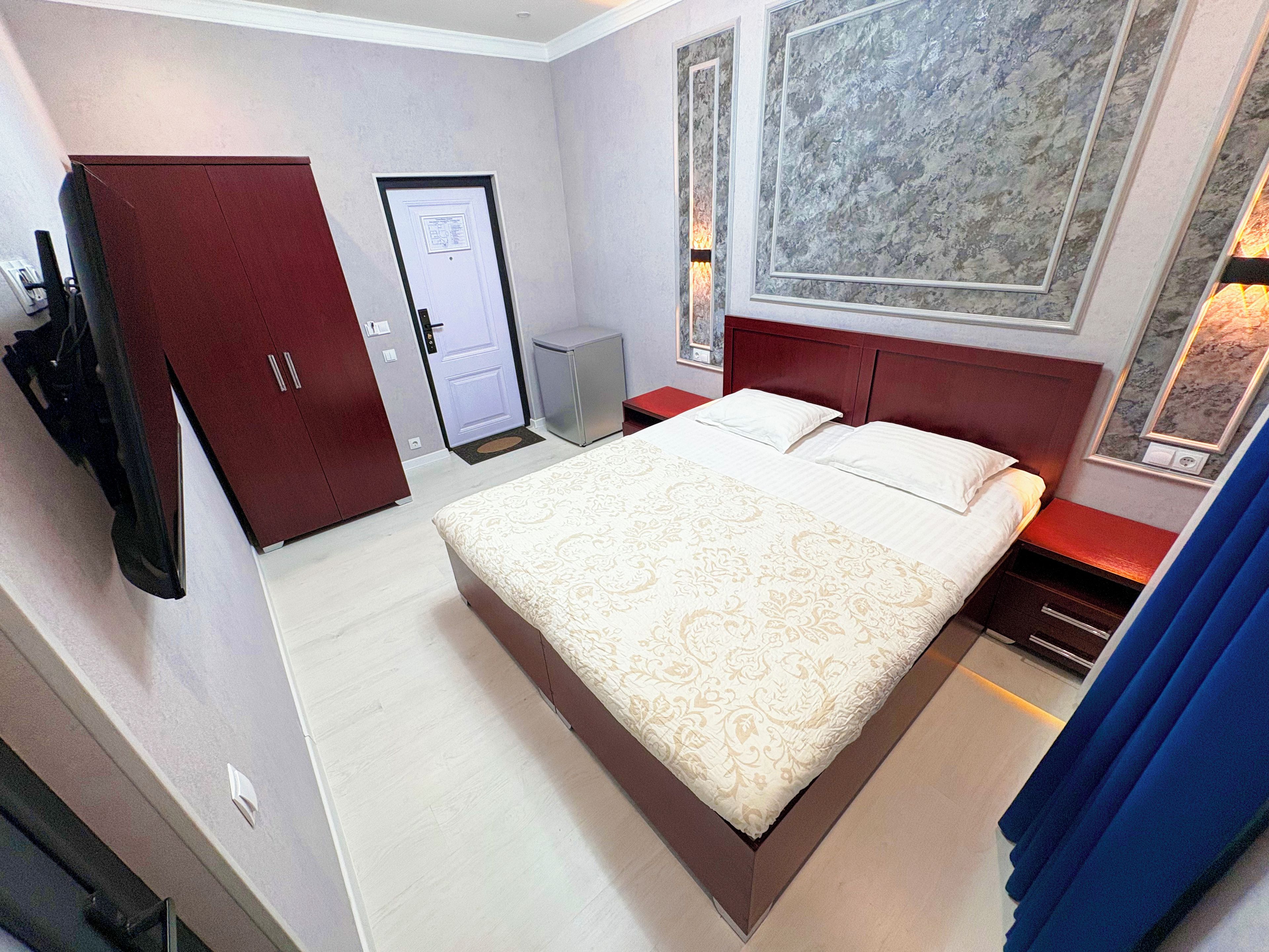 A hotel room with a large bed, a wardrobe, a desk, and a small cabinet.